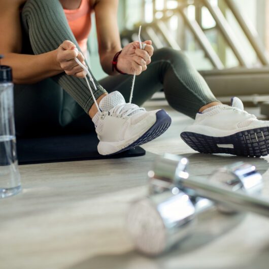 unrecognizable-athletic-woman-tying-sports-shoe-at-health-club